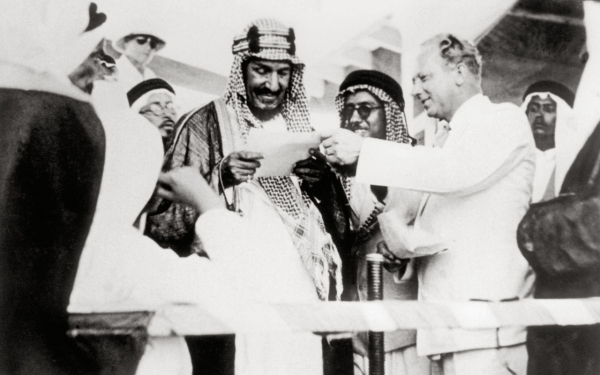 King Abdulaziz reading a congratulatory letter on the deck of a ship accompanied by ARAMCO President Floyd Ohliger. King Abdulaziz Foundation for Research and Archives (Darah)