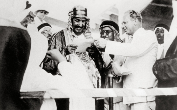 الملك عبدالعزيز يقرأ رسالة تهنئة على ظهر الباخرة برفقة رئيس أرامكو فلويد أوليجر. (دارة الملك عبدالعزيز)