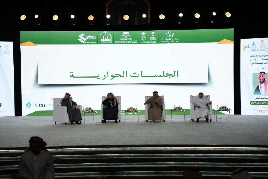 متحدثون يقفون على مسرح وخلفهم شاشة كبيرة.